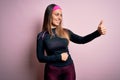 Young blonde fitness woman wearing sport workout clothes over isolated background Looking proud, smiling doing thumbs up gesture Royalty Free Stock Photo