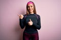 Young blonde fitness woman wearing sport workout clothes over isolated background Pointing to the back behind with hand and thumbs Royalty Free Stock Photo