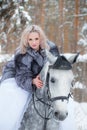 Young blonde in a fur coat, beautiful woman riding a light gray horse.