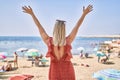 Young blonde girl on back view standing with hands raised up at the beach