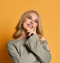Young blonde girl in torn jeans holds her chin and thinks over or dream about something on yellow background