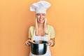 Young blonde girl cooking spaghetti winking looking at the camera with sexy expression, cheerful and happy face
