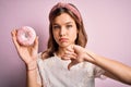 Young blonde girl eating sweet bakery sugar doughnut over pink isolated background with angry face, negative sign showing dislike