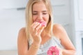 Young blonde girl eats pink donuts in home kitchen with taste emotions Royalty Free Stock Photo