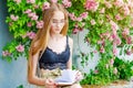 Young blonde girl in glasses reads a book against the background of a flowering rose bush Royalty Free Stock Photo