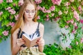 Young blonde girl in glasses reads a book against the background of a flowering rose bush