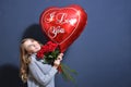 Young blonde girl in a gray sweater holding a bouquet of red roses and a heart balloon. Happy valentine day concept. young woman Royalty Free Stock Photo