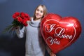 Young blonde girl in a gray sweater holding a bouquet of red roses and a heart balloon. Happy valentine day concept. young woman Royalty Free Stock Photo