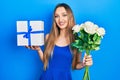 Young blonde girl holding anniversary present and bouquet of flowers smiling with a happy and cool smile on face Royalty Free Stock Photo