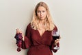 Young blonde girl holding branch of fresh grapes and red wine clueless and confused expression Royalty Free Stock Photo