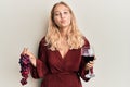 Young blonde girl holding branch of fresh grapes and red wine looking at the camera blowing a kiss being lovely and sexy Royalty Free Stock Photo