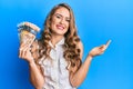 Young blonde girl holding canadian dollars celebrating achievement with happy smile and winner expression with raised hand