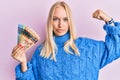 Young blonde girl holding canadian dollars strong person showing arm muscle, confident and proud of power