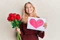 Young blonde girl holding heart draw and bouquet of roses smiling with a happy and cool smile on face Royalty Free Stock Photo