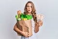 Young blonde girl holding paper bag with groceries and pounds puffing cheeks with funny face