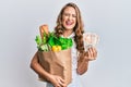 Young blonde girl holding paper bag with groceries and pounds smiling and laughing hard out loud because funny crazy joke