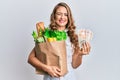 Young blonde girl holding paper bag with groceries and pounds winking looking at the camera with sexy expression, cheerful and