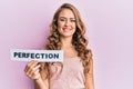 Young blonde girl holding paper with perfection message looking positive and happy standing and smiling with a confident smile Royalty Free Stock Photo