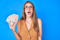 Young blonde girl holding united kingdom pounds angry and mad screaming frustrated and furious, shouting with anger looking up