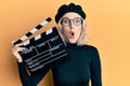 Young blonde girl holding video film clapboard scared and amazed with open mouth for surprise, disbelief face