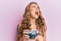 Young blonde girl holding vintage camera angry and mad screaming frustrated and furious, shouting with anger looking up Royalty Free Stock Photo