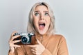 Young blonde girl holding vintage camera angry and mad screaming frustrated and furious, shouting with anger looking up Royalty Free Stock Photo