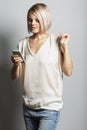 A young blonde girl in jeans and a white T-shirt with a phone in her hand looks at the screen. Blogging, online communication and