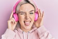 Young blonde girl listening to music using headphones sticking tongue out happy with funny expression Royalty Free Stock Photo