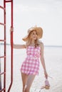 Young blonde girl look like a Barbie doll in pink tones and wide brim hat standing on beach Royalty Free Stock Photo