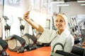 Young blonde girl making selfie photo on smartphone during workout break in gym Royalty Free Stock Photo