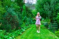 A young blonde girl in a pink dress with a red backpack on her back, a phone in her hand walks along a path and looking to the map Royalty Free Stock Photo