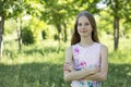 A young blonde girl in a pink t-shirt with arms crossed is standing against a background of green forest Royalty Free Stock Photo