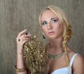 Young blonde girl posing in Slavic ethnic jewelry and with a bouquet of dried gilded flowers