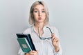 Young blonde girl reading a book and holding glasses puffing cheeks with funny face Royalty Free Stock Photo