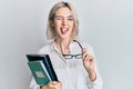 Young blonde girl reading a book and holding glasses sticking tongue out happy with funny expression Royalty Free Stock Photo