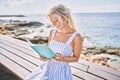 Young blonde girl reading book sitting on the bench at the beach Royalty Free Stock Photo