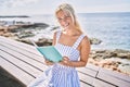 Young blonde girl reading book sitting on the bench at the beach Royalty Free Stock Photo