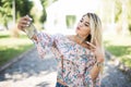 Young beautiful blonde girl relaxing in park, taking a selfie by mobile phone. Royalty Free Stock Photo