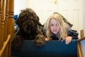 A young blonde girl and a shaggy black Labradoodle looking down from the top of the stairs