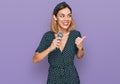 Young blonde girl singing song using microphone pointing thumb up to the side smiling happy with open mouth Royalty Free Stock Photo