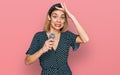 Young blonde girl singing song using microphone stressed and frustrated with hand on head, surprised and angry face Royalty Free Stock Photo