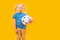 Young blonde girl with soccer ball against yellow background. Copy space, mockup. Child and football Royalty Free Stock Photo