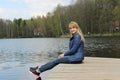 A young blonde girl is sitting on the shore of the lake