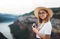 Young blonde girl in summer hat holds in hands on retro photo camera on background panorama horizin mountain and river landscape Royalty Free Stock Photo