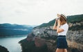 Young blonde girl in summer hat takes photo on retro camera on background panorama river horizin mountain landscape, hipster Royalty Free Stock Photo