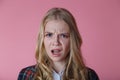 Young blonde girl with surprise and resentment on her face, close-up portrait on pink background