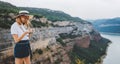 Young blonde girl takes photo of panorama landscape on retro camera during trip on mountains outdoors, hipster tourist in summer