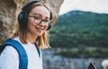 Young blonde girl tourist with backpack enjoying summer vacation listen music in headphones in nature, portrait smiling woman Royalty Free Stock Photo