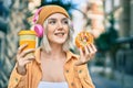 Young blonde girl using headphones having breakfast at the city