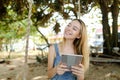 Young blonde girl using tablet and riding swing on sand, wearing jeans sundress. Royalty Free Stock Photo